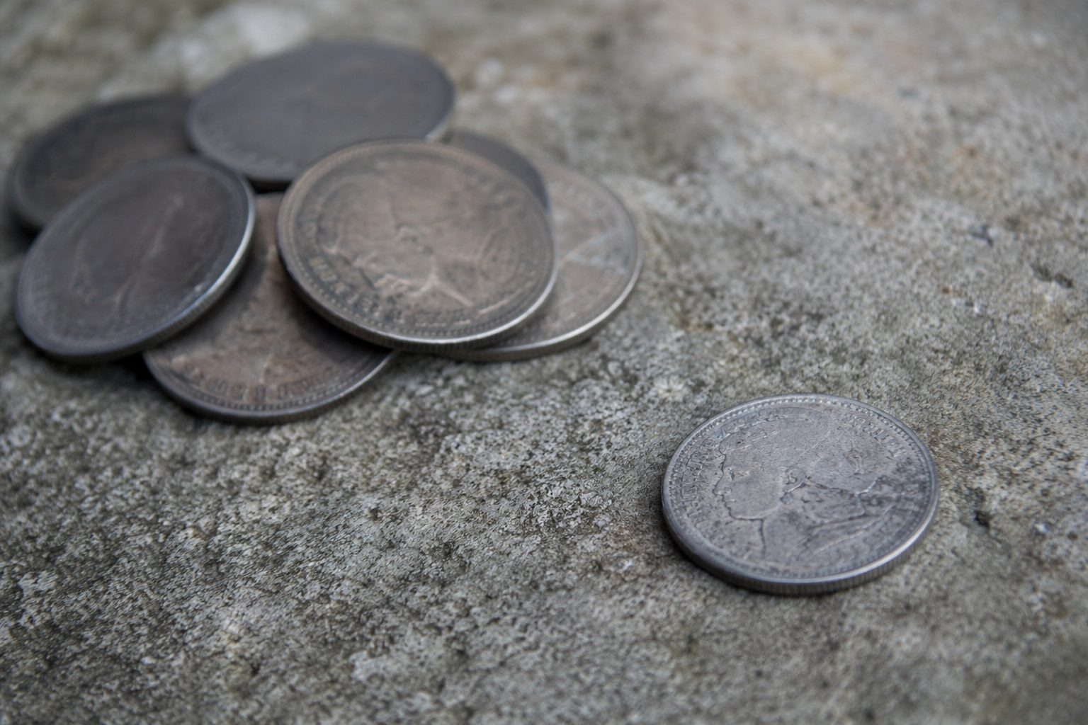 Old silver coins scattered on stone, representing Judas and the cost of money over relationship.